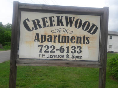 A picture of a street sign that says Creekwood Apartments along with the phone number of the property management company.